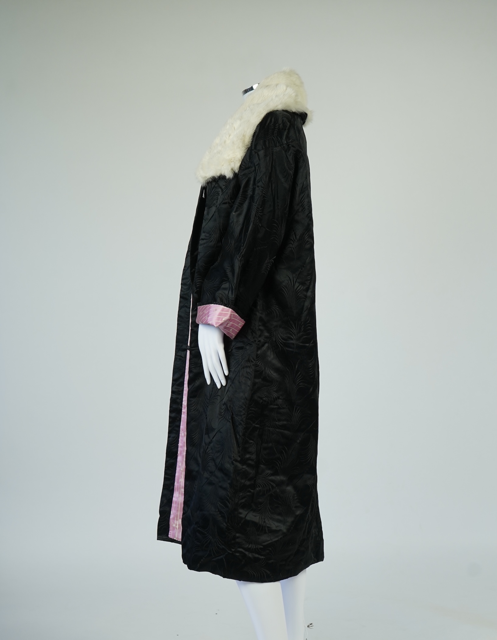 A 20th century ladies black silk damask opera coat, trimmed with a white fur collar and pink silk stripe brocade lining. 116cm from shoulder to hem. Condition - seams unstitched in places, small nick to black brocade by